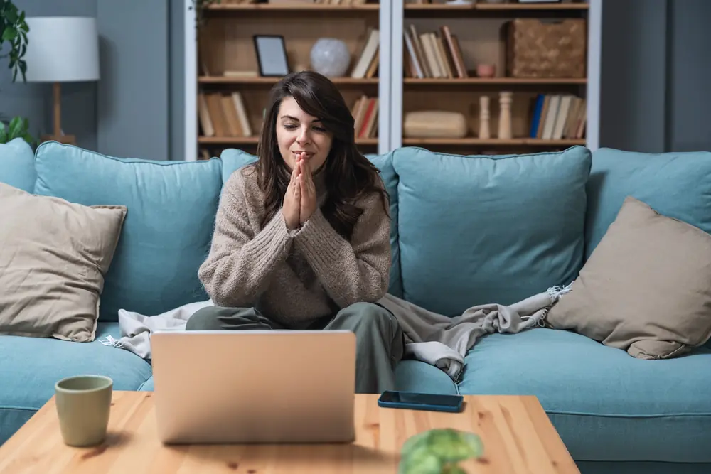 A woman sitting on her couch at home, talking with someone on her laptop